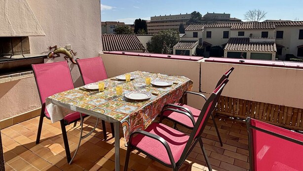 Un patio con una mesa lista para dos personas, una parrilla y vistas a edificios al fondo.
