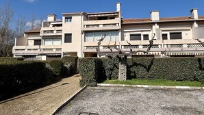 Un edificio residencial de varios pisos con balcones, camino de grava y seto.