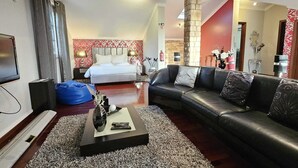 A modern hotel room with a large bed, a leather sofa, a flat-screen TV, and a blue bean bag.