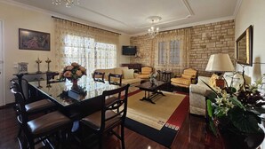 A spacious living room with a dining area, featuring a chandelier, a television, and a brick wall.