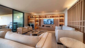 A modern living room with a large flat-screen TV, comfortable seating, a coffee table, and built-in shelves with ambient lighting. - Luxury Condo at Surf Residence with Ocean Views (Punta Mita)
