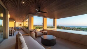 A modern, open-plan living area with a high ceiling, a ceiling fan, and a view of the sea. - Luxury Condo at Surf Residence with Ocean Views (Punta Mita)