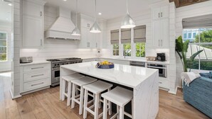 Una cucina moderna con mobili bianchi, una grande isola con sgabelli da bar e illuminazione a sospensione.