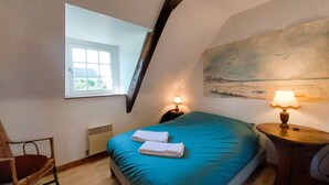 Un dormitorio con una cama, dos mesitas de noche, una silla, una ventana y un cuadro en la pared.