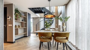 A modern dining area with a wooden table and two chairs, a black spiral staircase, and a large window with curtains. - Family Apartment w/ Bunk Beds (Delft)