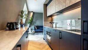 A modern kitchen with dark cabinetry, a marble countertop, and a built-in oven. There is a blue sofa and a potted plant in the background. - Family Apartment w/ Bunk Beds (Delft)
