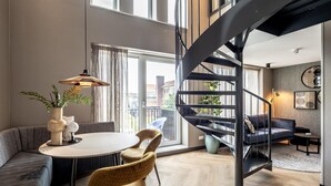 A modern living room with a spiral staircase, a round dining table, and a sofa. - Family Apartment w/ Bunk Beds (Delft)