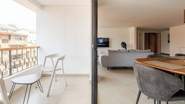 Un apartamento moderno con balcón, comedor, sala de estar con sofá y televisor.