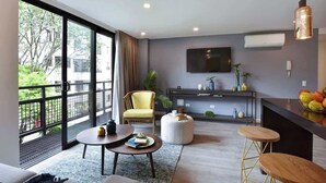 A modern living room with a sofa, a yellow armchair, a round coffee table, and a small side table. There is a TV mounted on the wall, a hanging pendant light, and a balcony with a view of greenery. - Villa del Peñon 301 - 2-Bed With Nice Balcony (Cali)