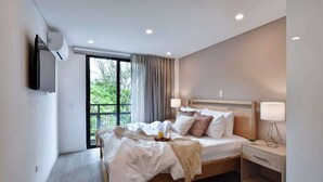 A modern hotel room with a large bed, bedside tables, a TV, and a view of greenery outside. - Villa del Peñon 301 - 2-Bed With Nice Balcony (Cali)