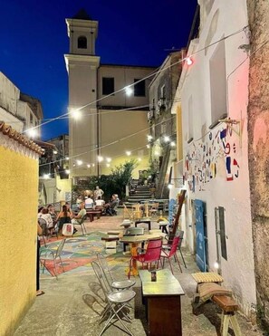 An outdoor dining area with tables and chairs, a mural on the wall, and a bell tower in the background. - Villa Lorena by the sea in Calabria (Saracena)
