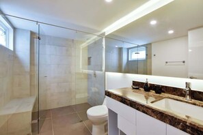 Un baño moderno con cabina de ducha acristalada, inodoro blanco y encimera de mármol con lavabo y espejo.