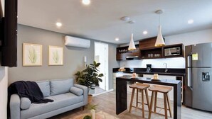 Une cuisine moderne avec un îlot central, des tabourets de bar et un canapé gris dans l’espace salon.
