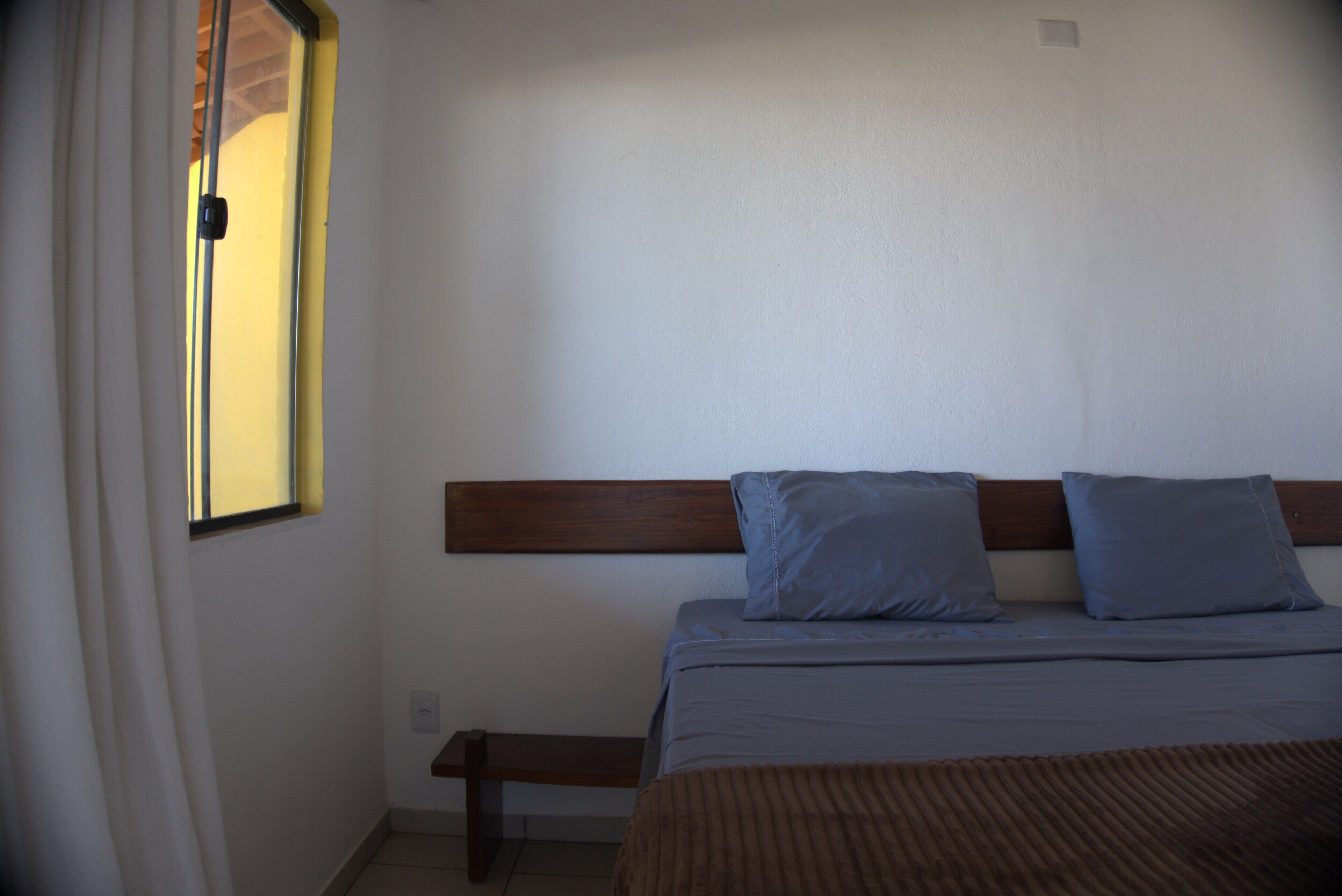 A bedroom with a bed, a wooden headboard, and a window with curtains.