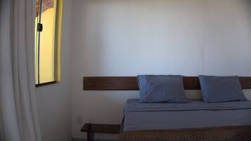 A bedroom with a bed, a wooden headboard, and a window with curtains.