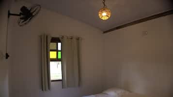 Quarto com cama, janela com cortinas, ventilador de teto e luminária pendente.
