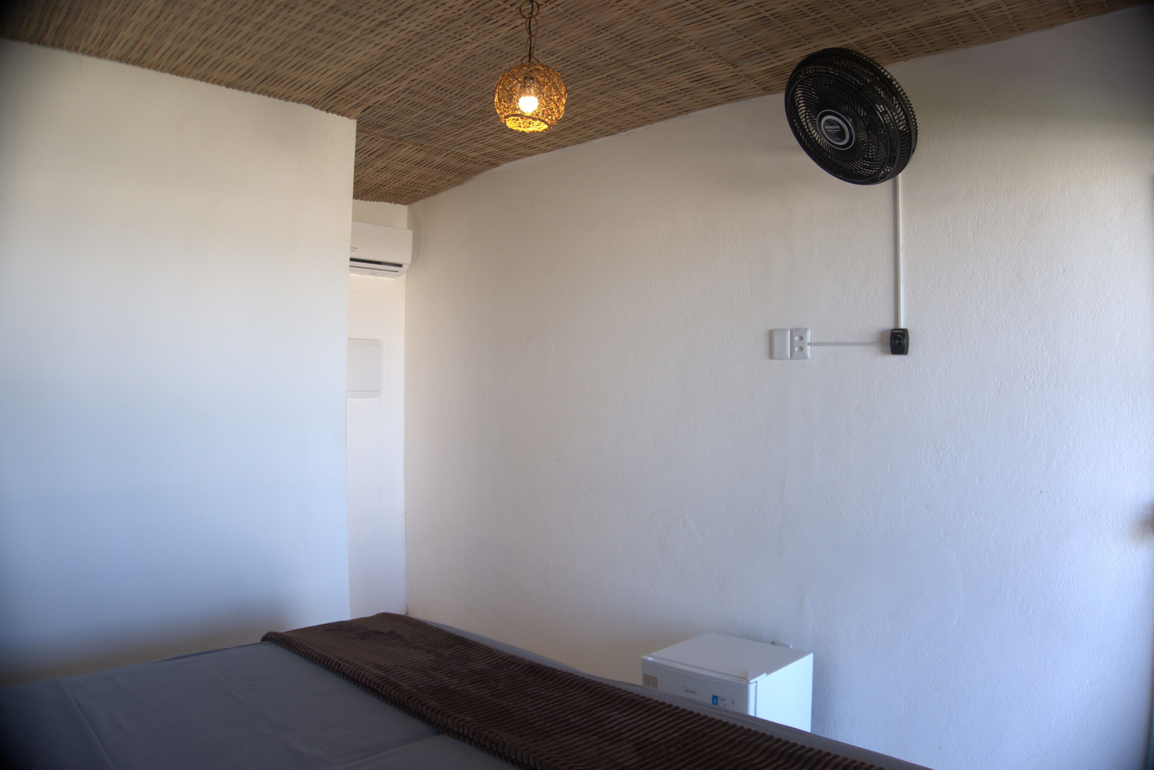 A bedroom with a bed, a ceiling fan, a wall-mounted light fixture, and a small white cabinet.