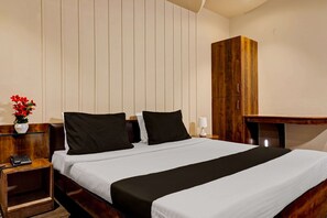A neatly made bed with a black and white bedspread, a wooden nightstand with a telephone, and a wooden wardrobe in a hotel room. - Elegant Stays in Downtown Bangalore (Pune)