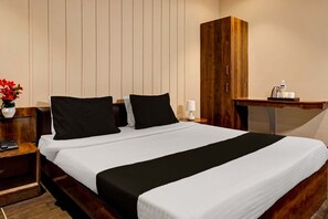A hotel room with a large bed, wooden headboard, a nightstand with a phone, a small table with a lamp, and a wooden wardrobe. - Elegant Stays in Downtown Bangalore (Pune)