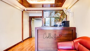Un espace d’accueil avec un comptoir en bois portant l’inscription « Collection », un canapé en cuir rouge et un plafond orné de motifs en bois.