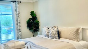 A neatly made bed with a grey blanket, a ceiling light fixture, a window with blinds, and a potted plant. - Seagrove-30A-3BR2BA house-bikes- beach gear- fire pit  (Santa Rosa Beach)