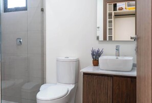 Bathroom features a glass-enclosed shower, toilet, and sink with a wooden cabinet below.