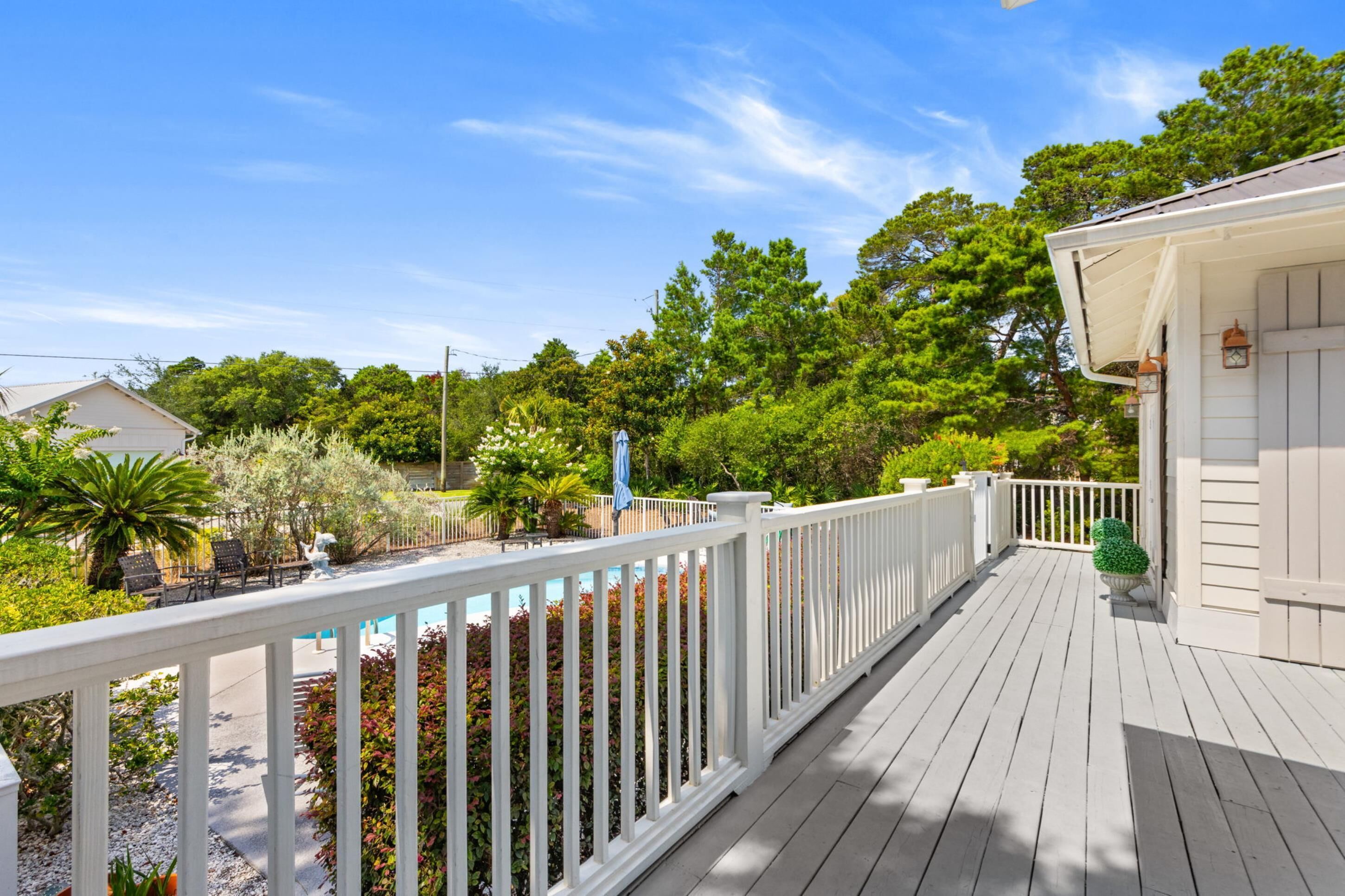 A wooden deck with a white railing, surrounded by greenery and trees.