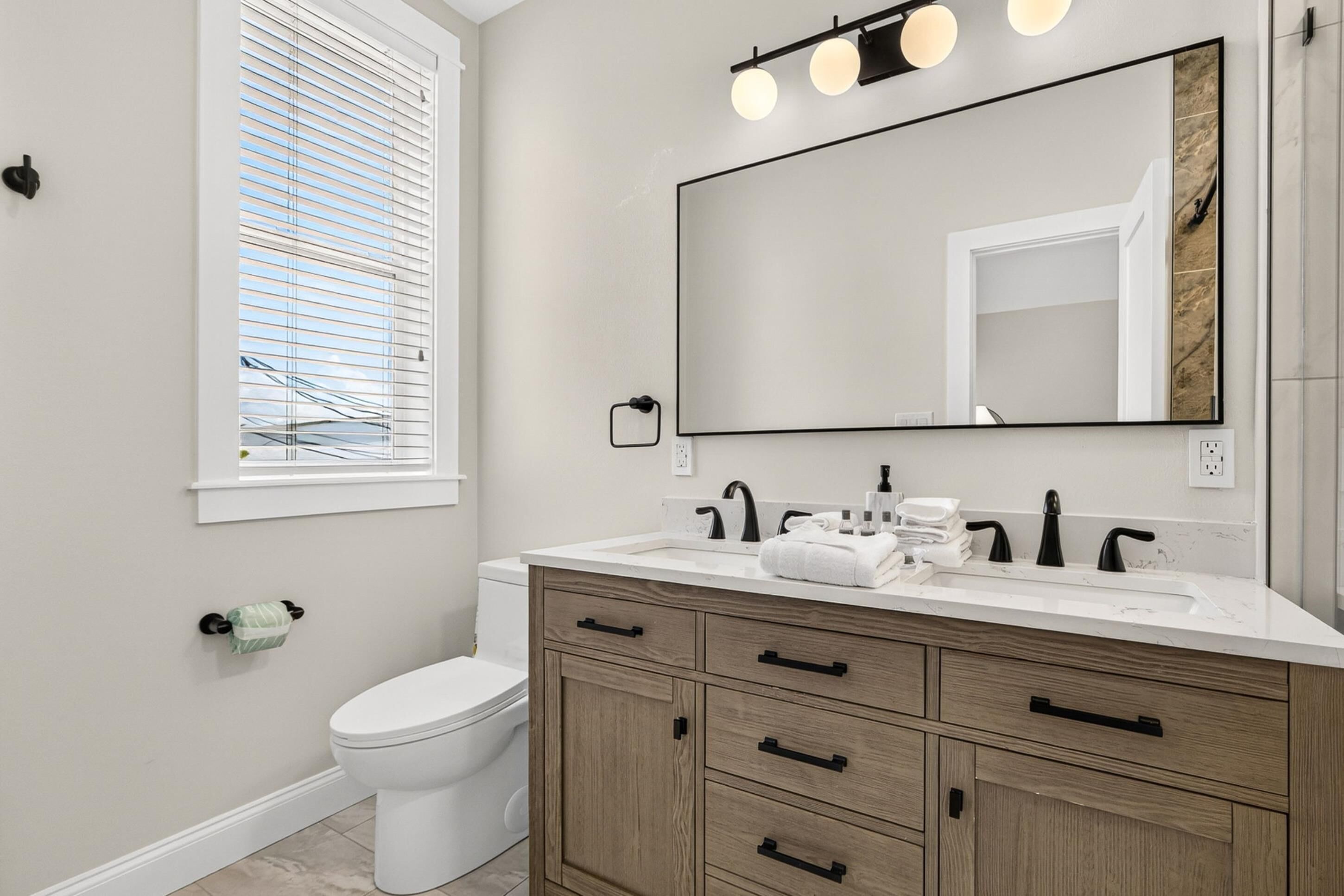 A bathroom with a toilet, a sink with a mirror above it, and a window with blinds.