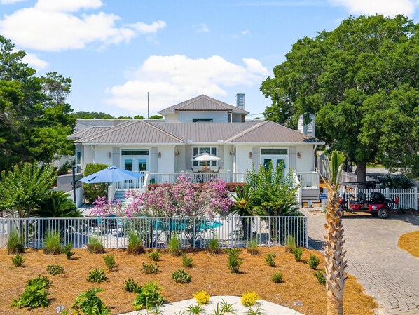 A two-story house with a front porch, a swimming pool, and a fenced garden area.