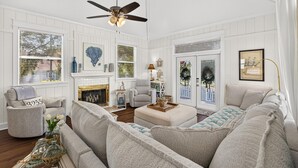Ein geräumiges Wohnzimmer mit Kamin, Deckenventilator und großem Fenster mit Jalousien.