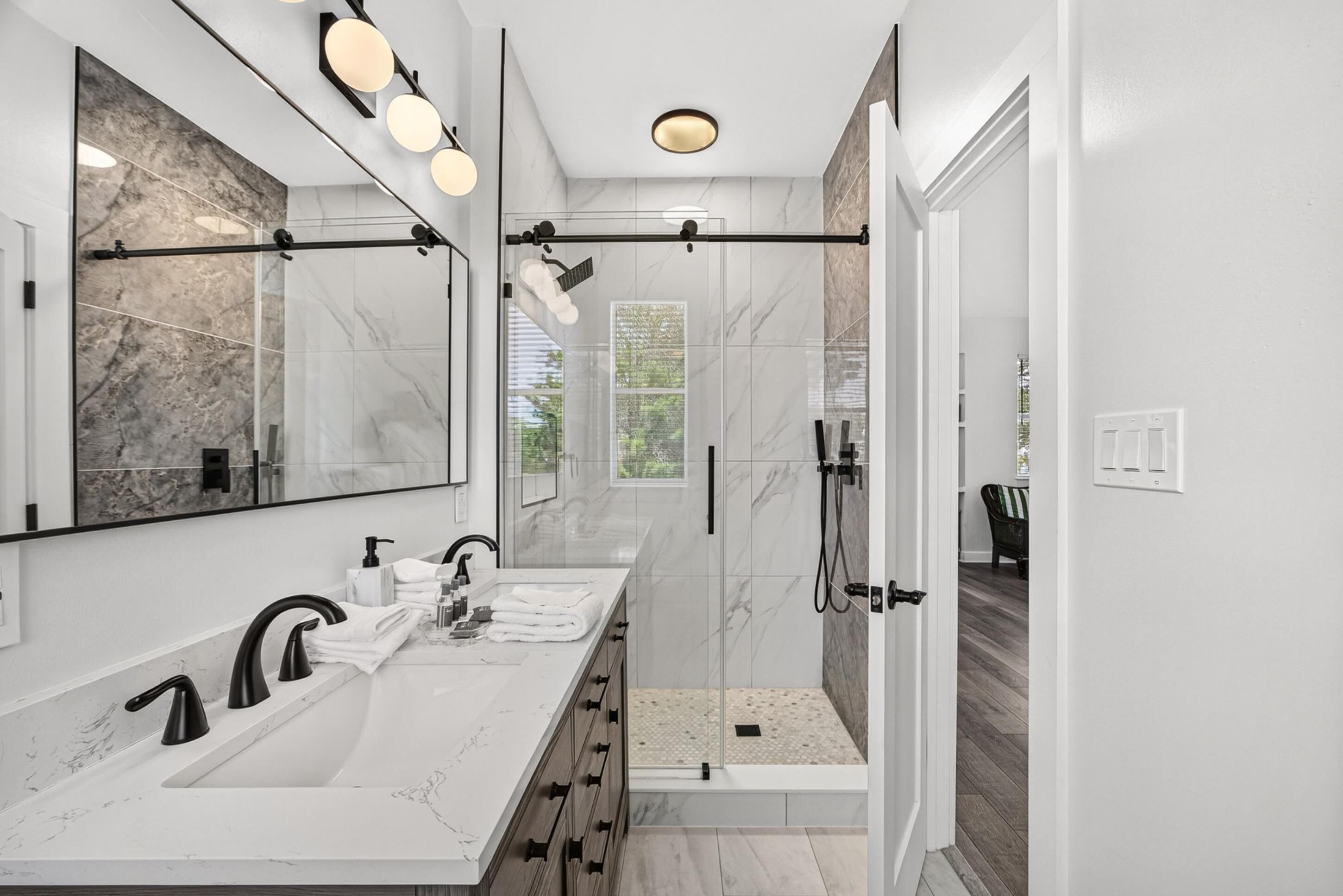 A modern bathroom with two sinks, a large mirror, and a glass-enclosed shower area.