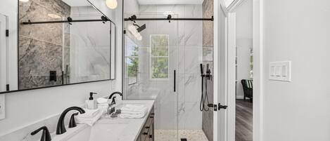 A modern bathroom with two sinks, a large mirror, and a glass-enclosed shower area.