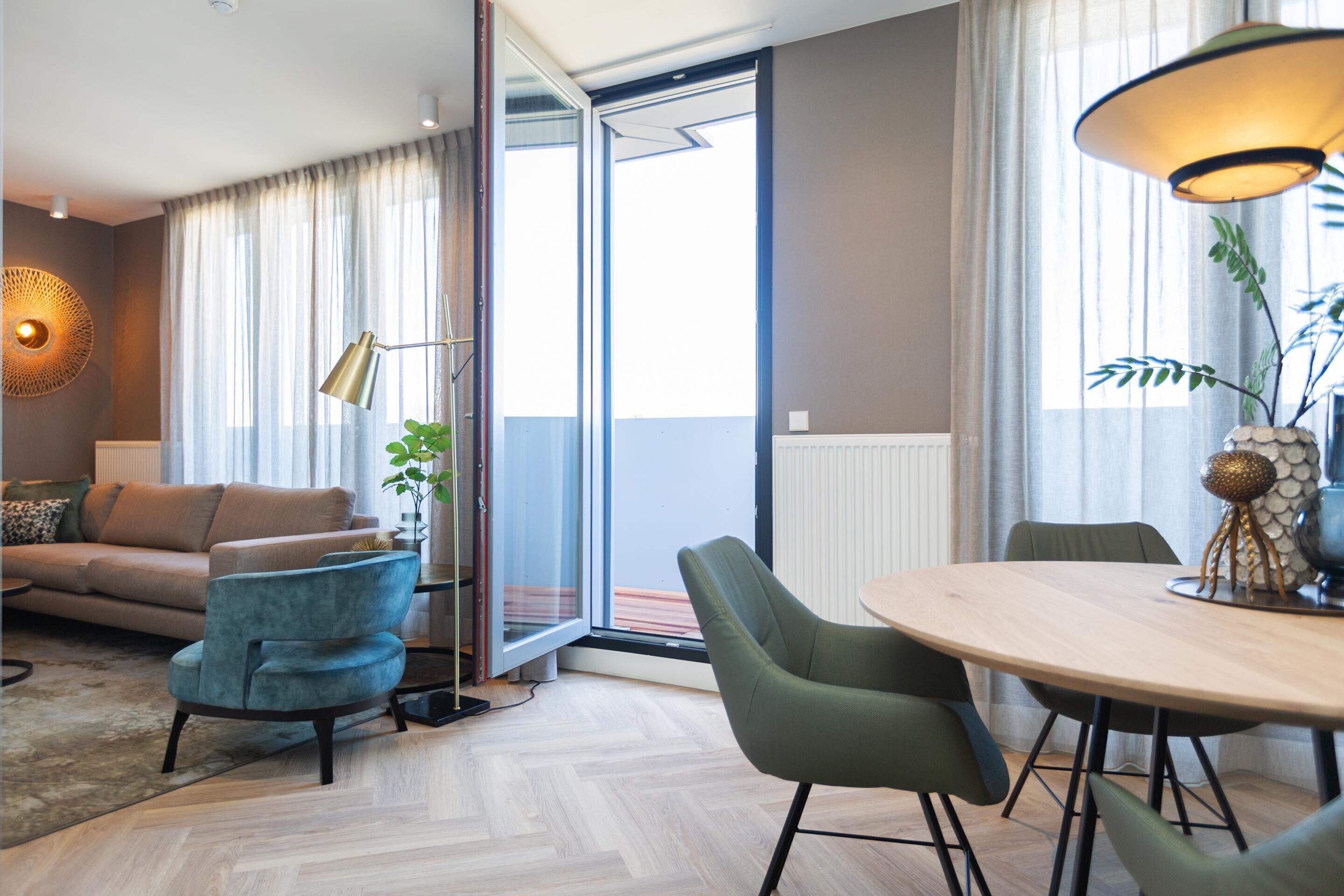 A modern living room with a sofa, chairs, a dining table, and a large window with curtains.