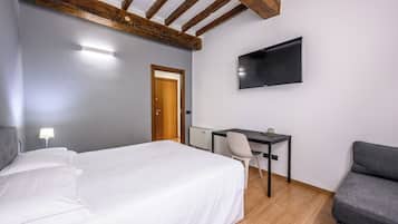 Un dormitorio con cama, escritorio, silla, televisor y puerta.