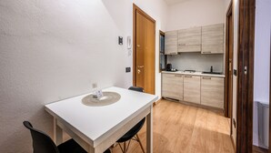 A small, compact room with a white table and chairs, a wooden door, and a kitchenette with light wood cabinets. - Emilia Studios 3 (Modena)