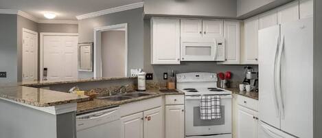 Una cocina moderna con armarios blancos, microondas integrado, estufa y refrigerador.