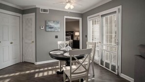 Un coin repas avec un ventilateur de plafond, une table avec des chaises et une vue sur une autre pièce, accessible par une porte.