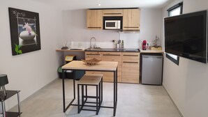 A modern kitchen with wooden cabinets, a microwave, a sink, and a dishwasher. There is a dining table with stools and a TV mounted on the wall.