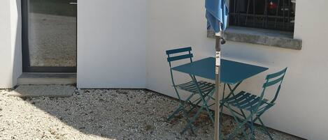A patio area with a table and chairs, a blue umbrella, and a door.