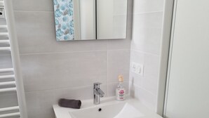 A bathroom with a white sink, wooden cabinet, and a mirror above it.