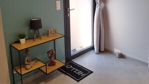 A room with a teal wall, a wooden shelf with a lamp, a calendar, and a 'HELLO' mat.
