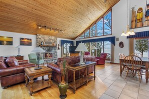 A spacious living room with a high ceiling, wooden floors, and large windows. There are leather sofas, a dining table with chairs, and a fireplace. - Home on the Bay in Door County (Luxemburg)
