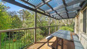 A covered outdoor deck with a bench, surrounded by a metal railing, overlooking a lush garden.
