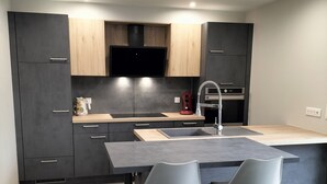 A modern kitchen with dark cabinetry, a wooden countertop, and two grey chairs. - Large 8-person house with sauna, terrace and garden close to Colmar (Sainte-Croix-en-Plaine)
