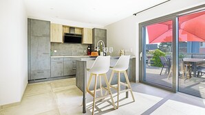 A modern kitchen with grey cabinets, a built-in oven, and a large window with a red umbrella. - Large 8-person house with sauna, terrace and garden close to Colmar (Sainte-Croix-en-Plaine)