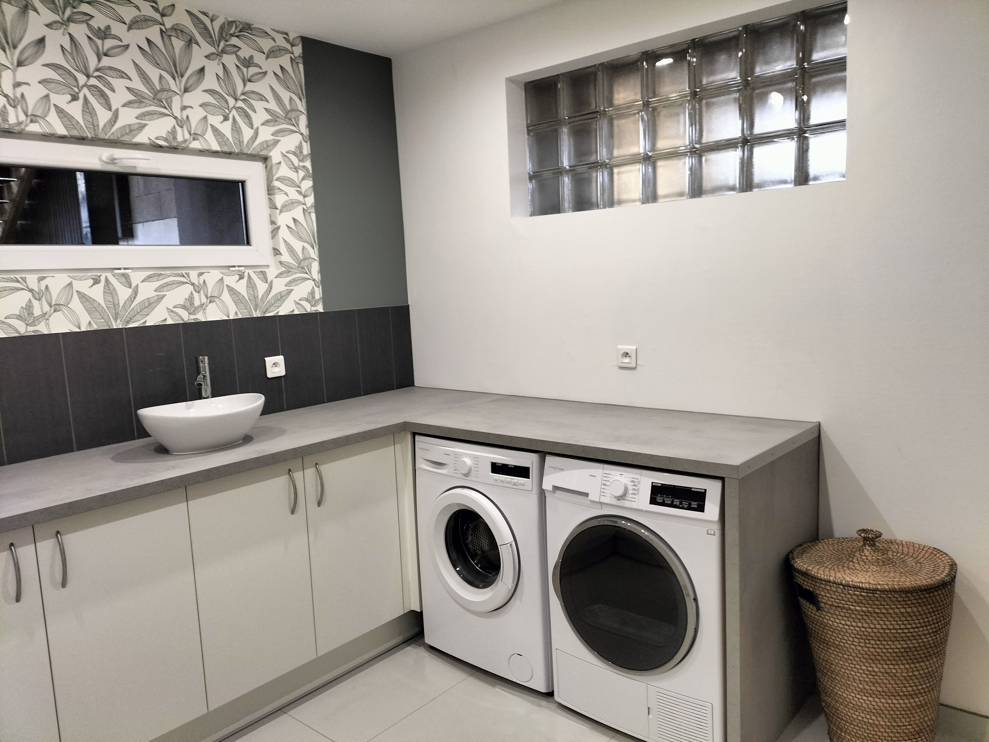 A compact laundry room with a washing machine, a sink, and a window with blinds.