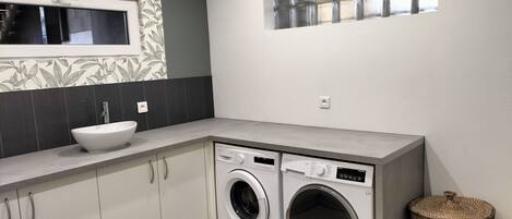 A compact laundry room with a washing machine, a sink, and a window with blinds.