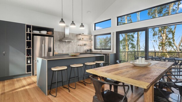 Una cocina moderna con una isla central, taburetes de bar y una mesa de comedor con sillas.