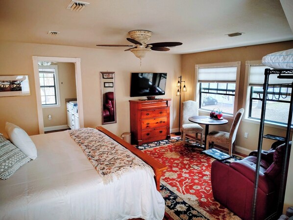 Une chambre d’hôtel avec un lit, une commode, une télévision, une chaise, une petite table et une fenêtre donnant sur un paysage agréable.