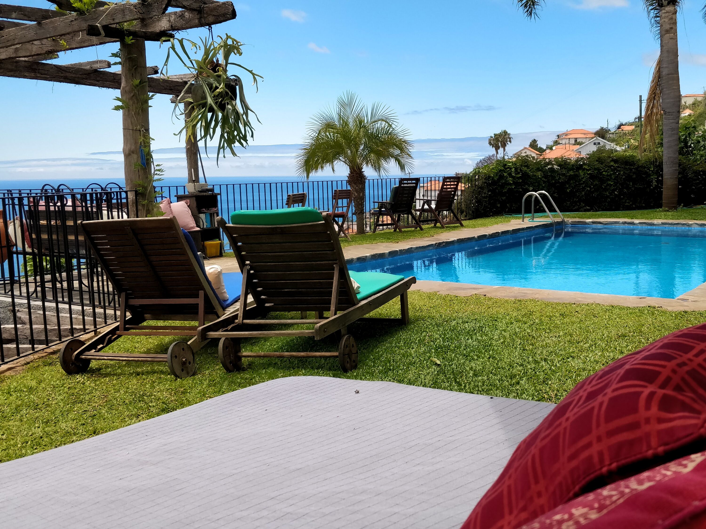 A poolside area with lounge chairs, a wooden pergola, and a view of the ocean.